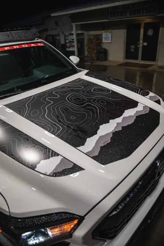 White truck with topographic hood decal featuring the 2024+ Tacoma Apex Hood Stamp