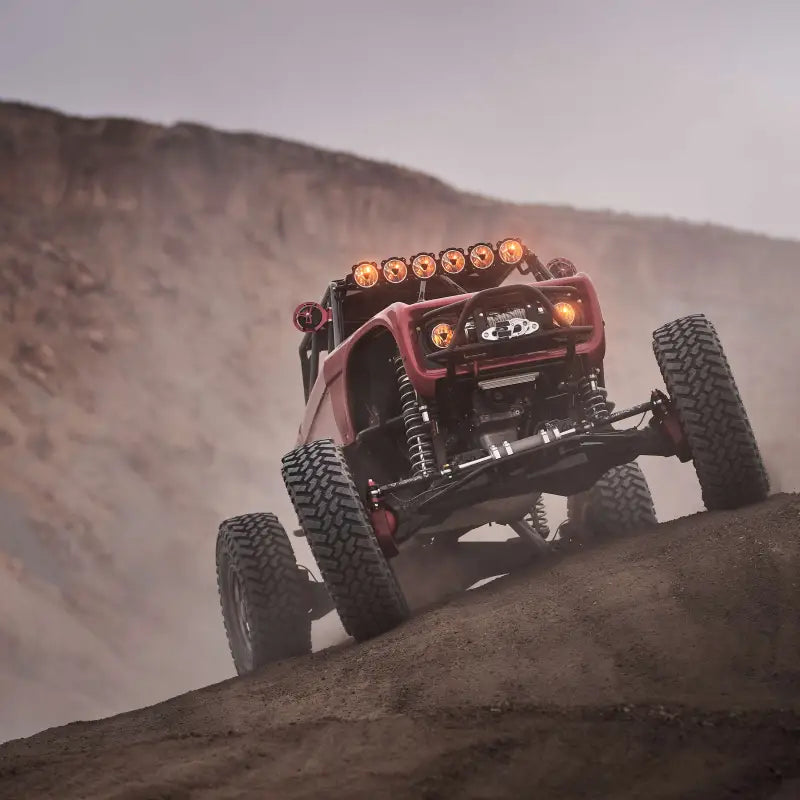 Red off-road vehicle ascending a steep hill with Titan™ LED Light Bar, highlighting its powerful illumination.