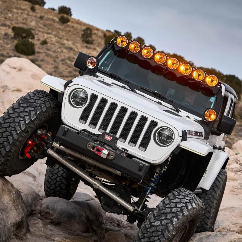 White Jeep Rubicon equipped with the 50-inch Gravity Titan LED Light Bar, climbing rocky terrain with amber lighting.