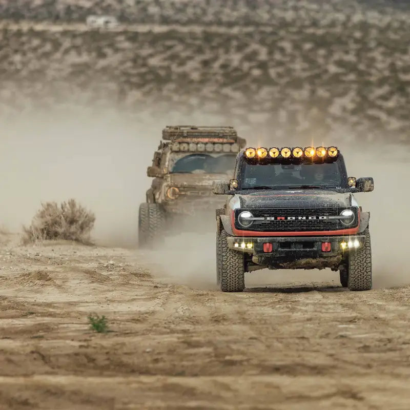 Two Ford Broncos driving through a dusty trail, both equipped with the 50-inch Gravity Titan LED Light Bar for off-road lighting.