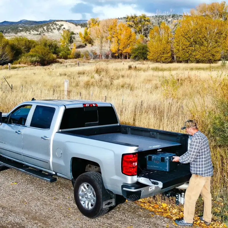 Man loading gear under the 6' Cot - Portable Air-Deck in a truck bed, demonstrating storage efficiency and outdoor utility.