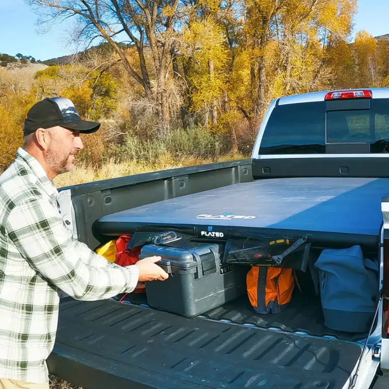 Man organizing gear under the 6' Cot - Portable Air-Deck in a truck bed, highlighting its storage capacity and practical design.