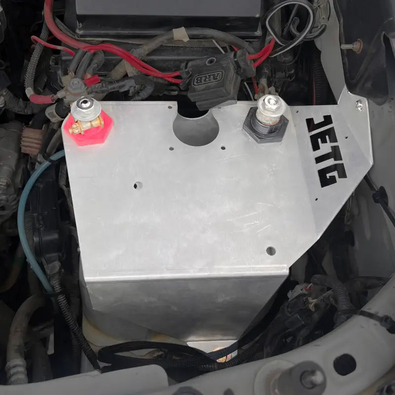 Engine bay view of a Toyota Tacoma with the JETG Designs battery relocate kit installed, featuring a sturdy aluminum bracket.