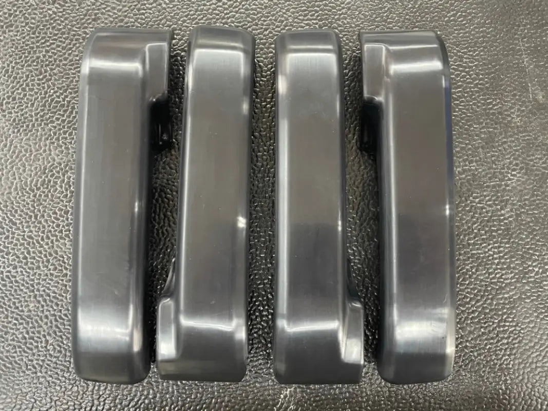 Close-up of four Tundra blackout door handle covers on a textured surface, highlighting their smooth black finish and durable design.