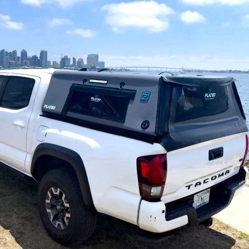 White truck with the CAP Mid-Size 5' Bed Air-Topper parked by a waterfront, showcasing its sleek design and compatibility with Tacoma models.