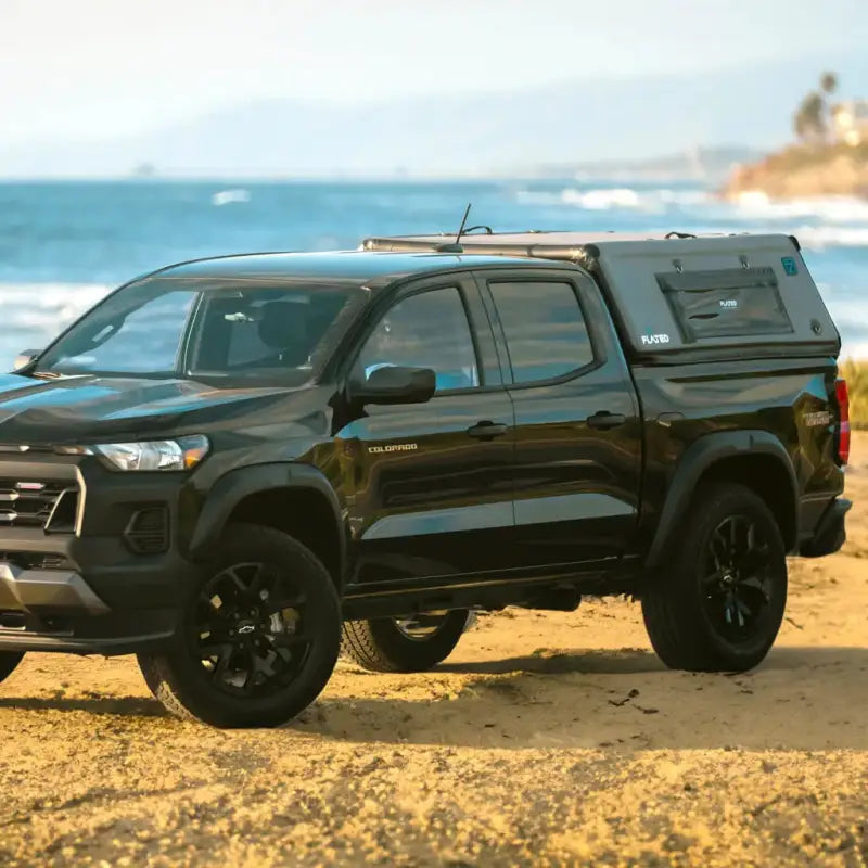 Black truck equipped with the CAP Mid-Size 5' Bed Air-Topper parked on a beach, emphasizing its versatility and outdoor utility.