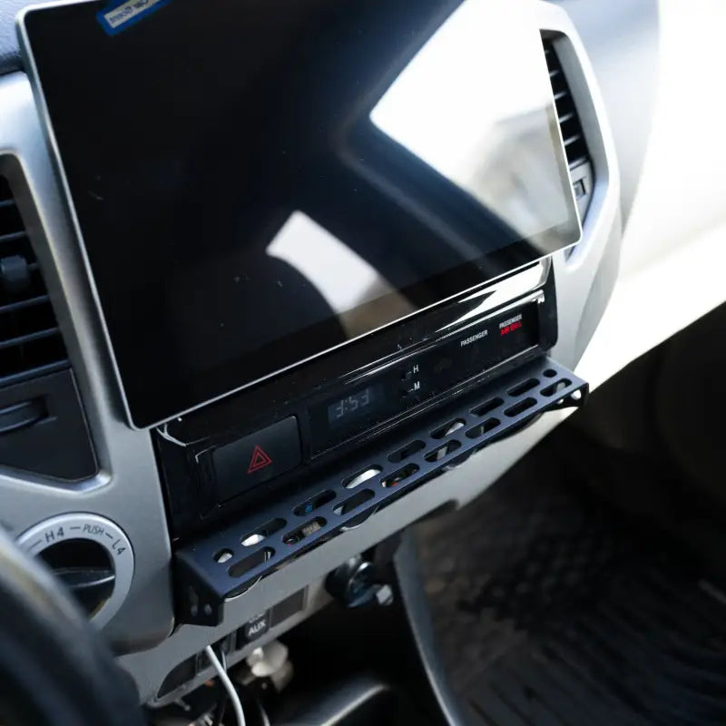 Tacoma center console modular accessory mount installed below the dashboard screen, featuring a laser-cut aluminum design.