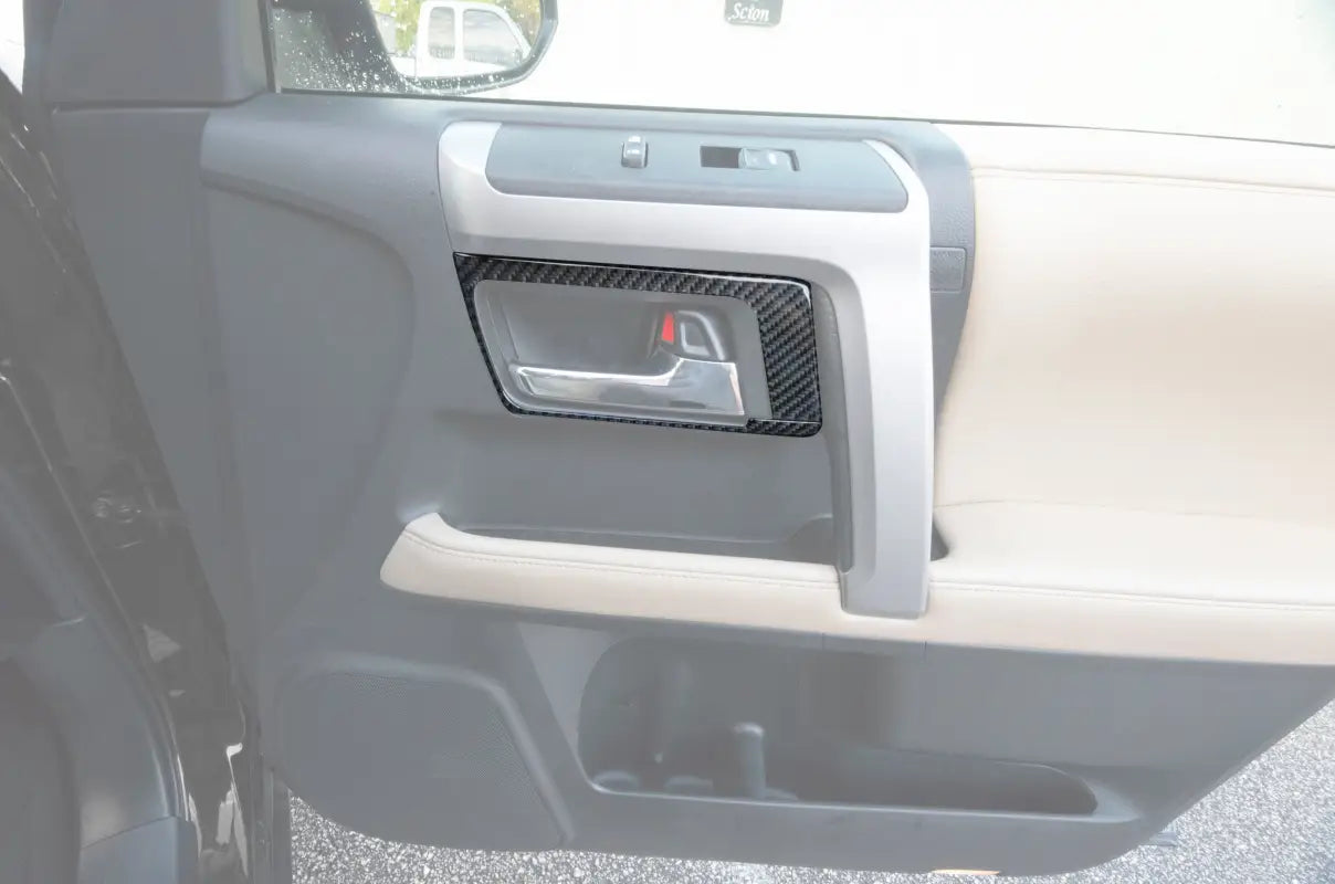 Carbon fiber door handle accent trim installed on a 2014-2024 Toyota 4Runner interior door panel, enhancing the design.