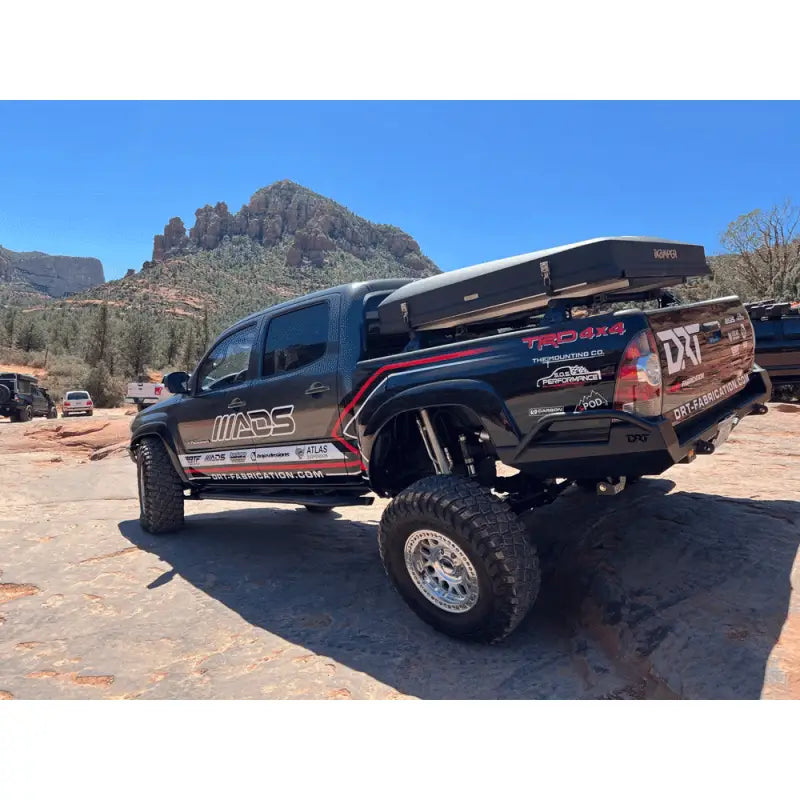 Side view of a 2005-2015 Toyota Tacoma equipped with a DRT high clearance rear bumper, featuring off-road modifications and a rooftop tent.