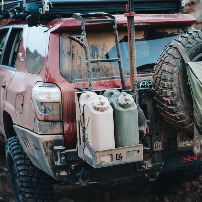 Dual Jerry Can Carrier mounted on a red off-road vehicle with muddy exterior, holding two jerry cans securely.