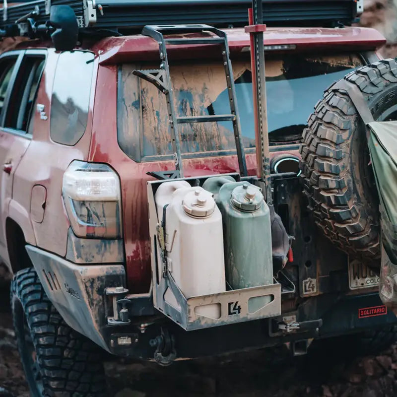 Dual Jerry Can Carrier mounted on a red off-road vehicle with muddy exterior, holding two jerry cans securely.