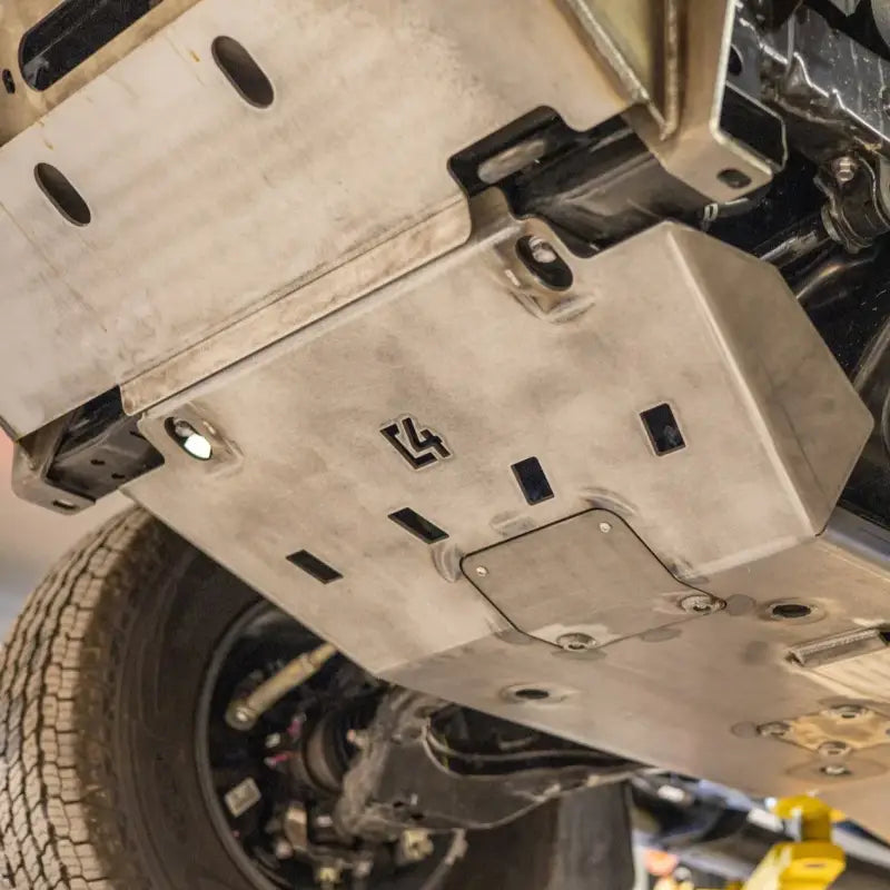 Underneath view of a Tacoma front skid plate installed on a vehicle, showcasing CNC steel construction and bolt-on design for 2005+ Toyota models.