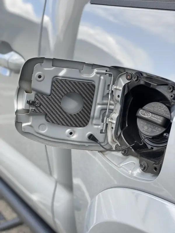Carbon fiber-style gas cap holder insert for Toyota Tacoma 2005-2023, installed in the fuel door area.