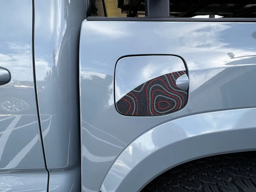 Gas lid protection overlay with black texture and topographic map design in red and gray, fits 2016-2023 Toyota Tacoma.