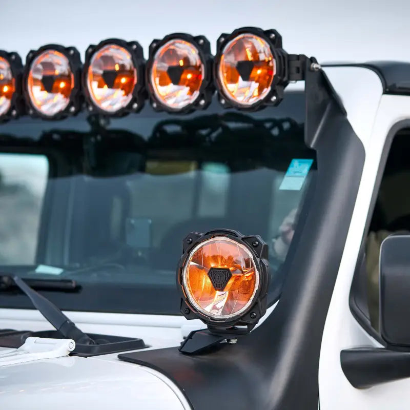 White Jeep with Gravity Titan 6-inch LED lights in amber mode, mounted on the roof and bumper for off-road use.