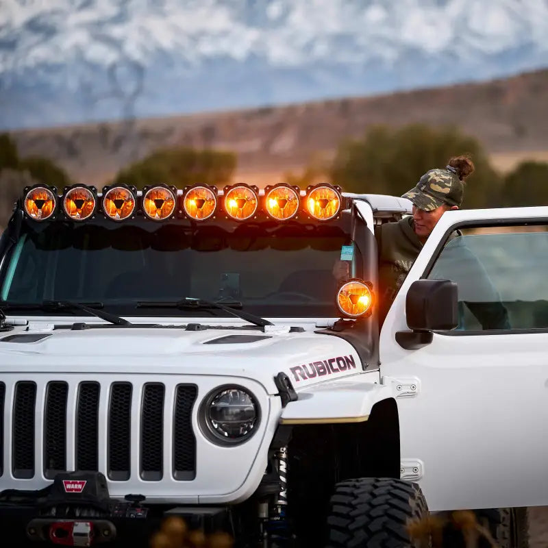 Driver adjusting Gravity Titan 6" LED Spot Beam light on a white Rubicon, set against a mountain backdrop.