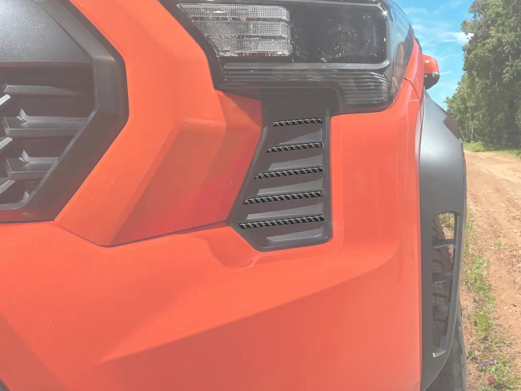 Grille side line accent trim installed on a 2024-2025 Toyota Tacoma in Inferno orange, showcasing a sleek carbon fiber design.