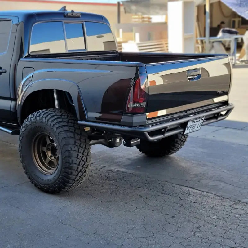 Close-up of 2005-2015 HC Rear Tube Bumper installed on a Toyota Tacoma, showcasing light pod tabs, bed reinforcement, and sleek body filler panels.