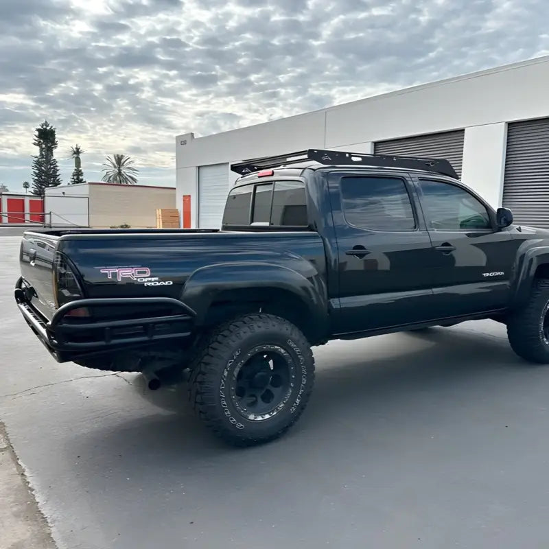 Tacoma HC Rear Bumper for 2005-2015 models featuring high clearance and tubular construction. Shown on a black Toyota Tacoma with off-road tires.