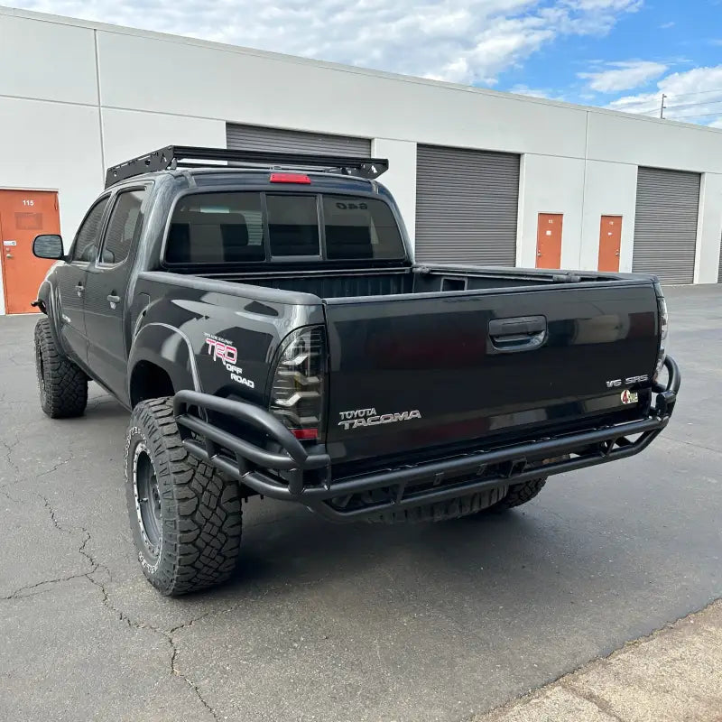 2005-2015 Tacoma HC Rear Bumper in black with high clearance design, tubular build, and hitch receiver. Installed on a lifted black Toyota Tacoma.