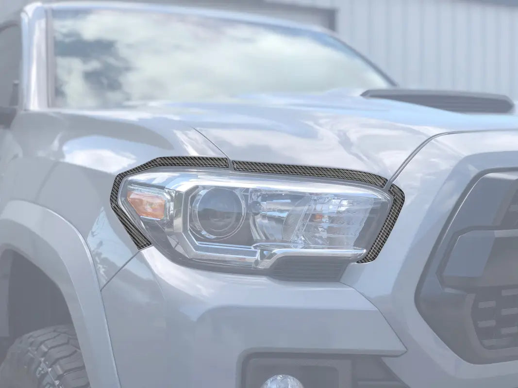 Carbon fiber headlight accent overlays installed on a 2016-2023 Toyota Tacoma, enhancing the vehicle's front-end appearance.