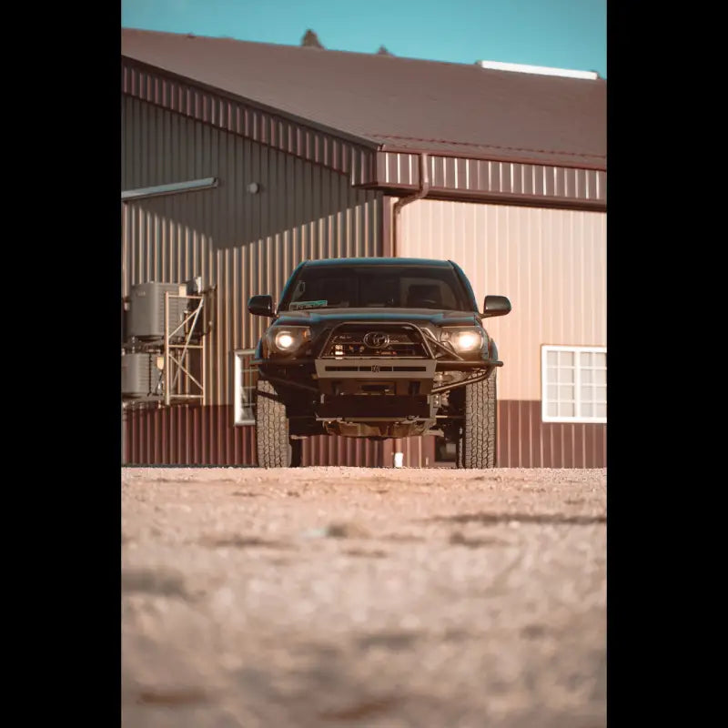 Toyota Tacoma with hybrid front bumper, bolt-on fit for 2012-2015 models, parked in front of a metal building.