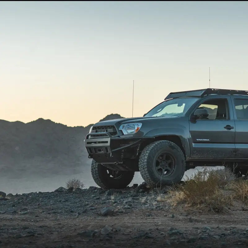 Side view of Toyota Tacoma featuring a hybrid front bumper, designed for 2012-2015 models, on a rugged landscape.