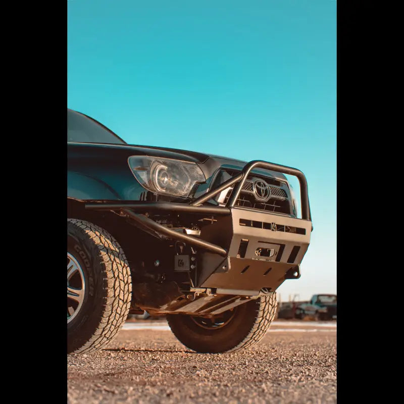 Angled view of Toyota Tacoma with hybrid front bumper, winch-ready and bolt-on fit for 2012-2015 models, in a parking lot.