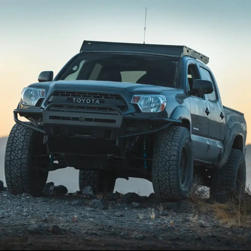 Toyota Tacoma with hybrid front bumper, winch-ready, bolt-on fit for 2012-2015 models, parked on rocky terrain.