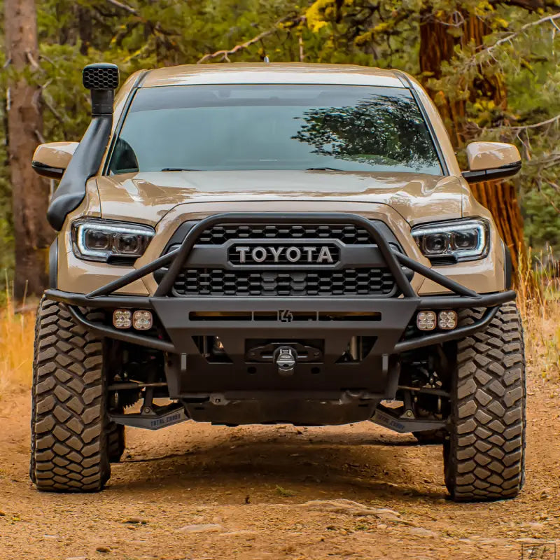 Front view of a 3rd Gen Tacoma with a hybrid steel front bumper, showcasing winch mount and light bar integration in a forest environment.