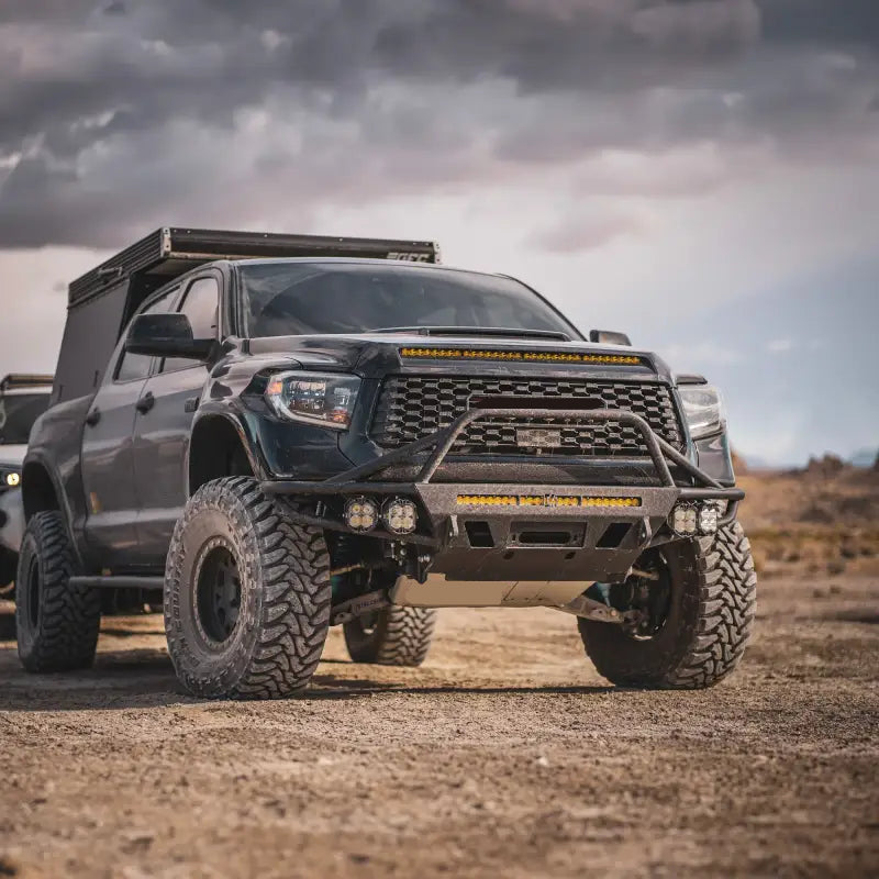 Black Toyota Tundra with hybrid front bumper, winch mount, LED bar, and fog lights, designed for 2014-2021 models, off-road setup.