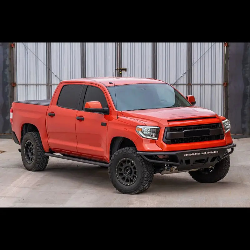 Orange Toyota Tundra with hybrid front bumper, LED bar, and off-road tires, designed for 2014-2021 models, parked on concrete.