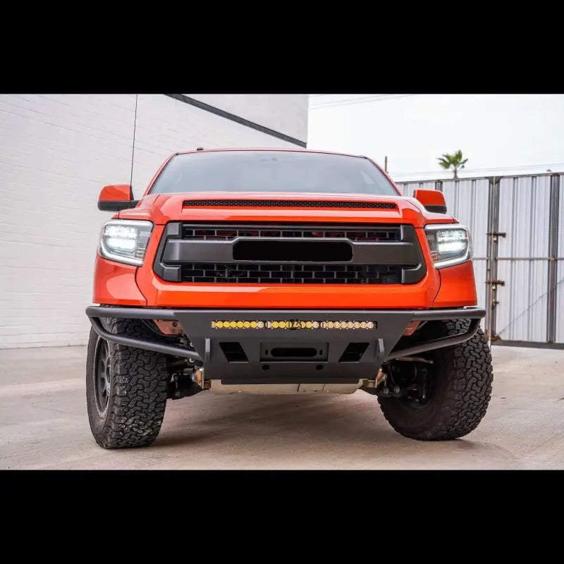 Front view of orange Toyota Tundra with hybrid front bumper, LED bar, and fog lights, designed for 2014-2021 models.