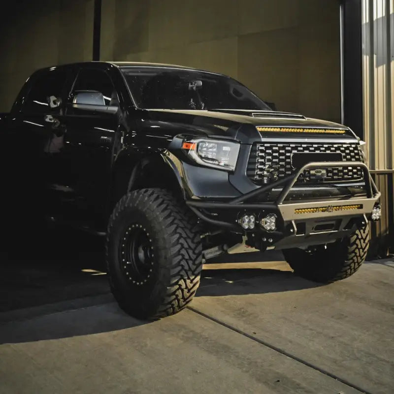 Black Toyota Tundra featuring a hybrid front bumper with LED bar and fog lights, optimized for 2014-2021 models, parked indoors.