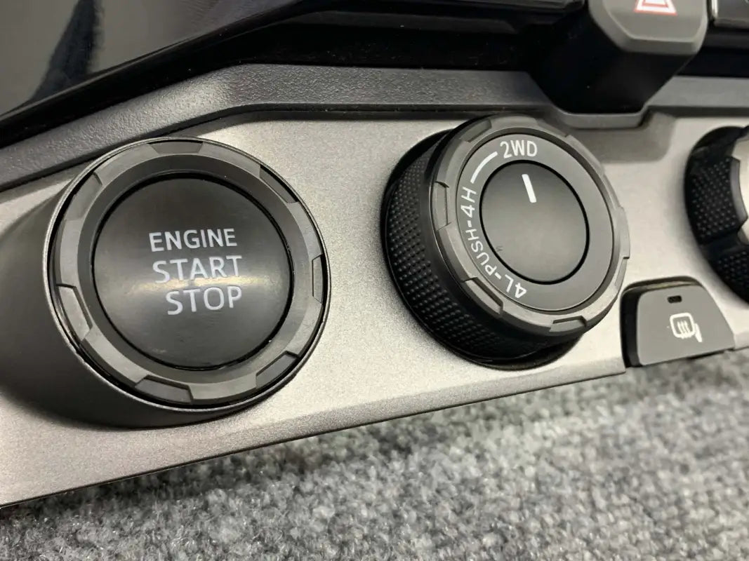 Close-up of black chrome delete trim installed around the start-stop button and control knobs in a Toyota Tacoma.