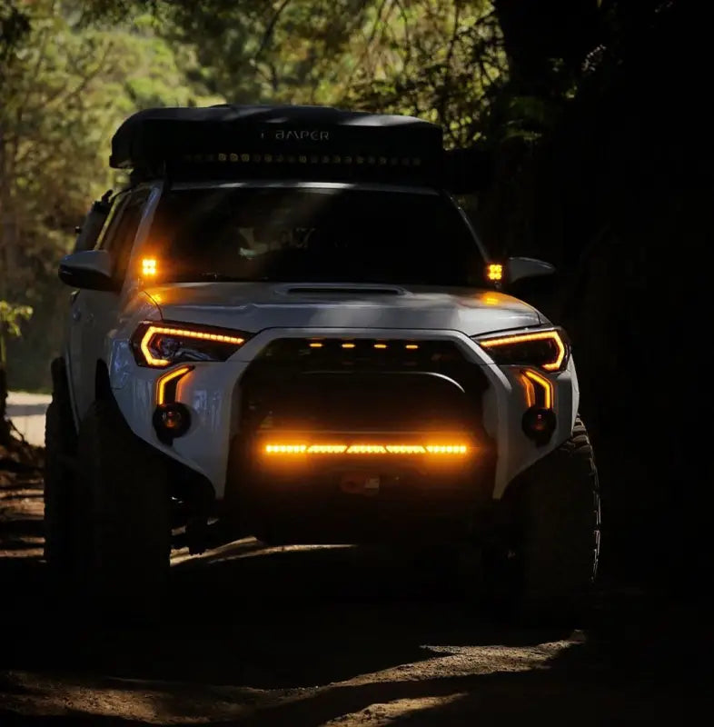 Toyota 4Runner with LED DRL Fang Light Bezel Kit in amber, illuminated in a forest setting, highlighting rugged design and improved visibility.