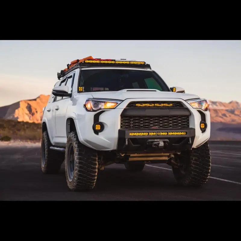 White 5th Gen 4Runner with Lo Pro Winch Bumper, LED light bars, and off-road tires, parked in a desert landscape.