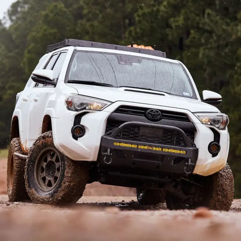 White 5th Gen 4Runner with Lo Pro Winch Bumper and LED light bar, driving through muddy terrain with off-road tires.