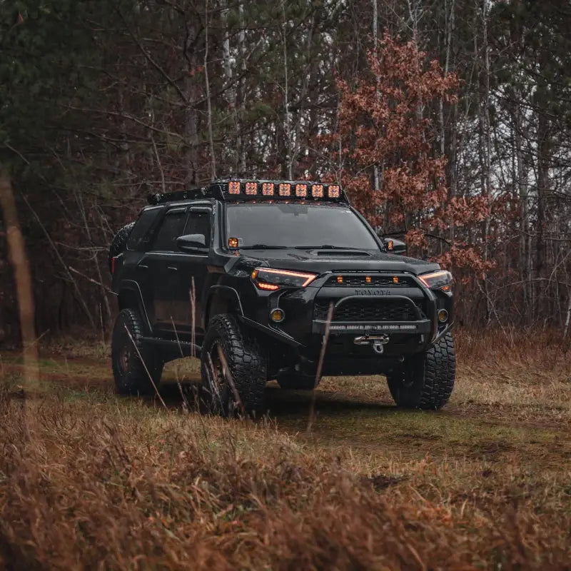 Black 5th Gen 4Runner equipped with Lo Pro Winch Bumper and LED light bars, parked in a wooded area with off-road tires.
