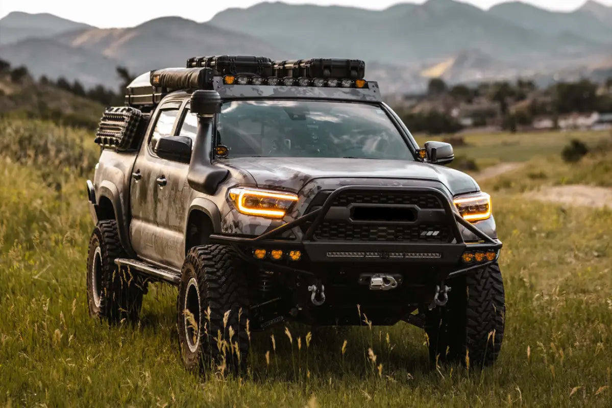 Lifted Toyota Tacoma equipped with Morimoto HXB 4Banger Ditch Light Kit and other off-road accessories, parked in a grassy field.