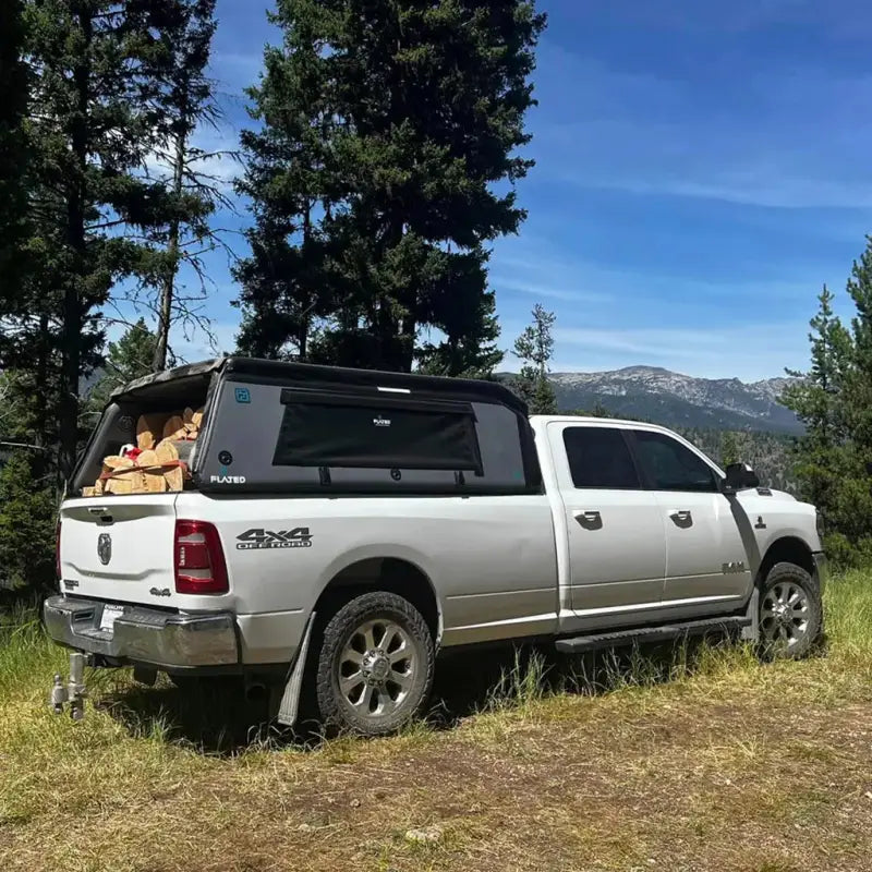 White truck with MR Full-Size Truck Topper loaded with firewood, parked in a forest, showcasing its storage capacity and outdoor utility.