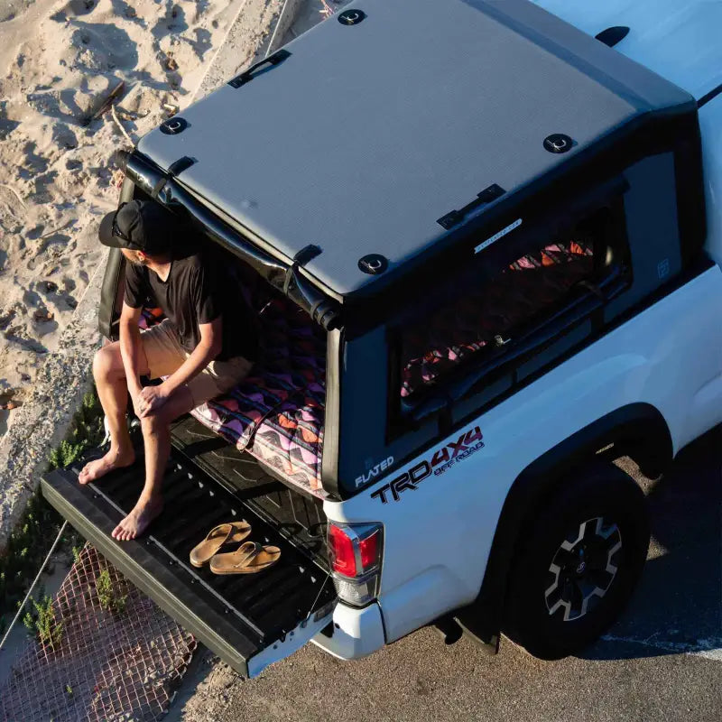 MR - Mid-Size 6'-Long Bed inflatable truck shell on a white truck with a person sitting on the tailgate, highlighting its camping functionality.