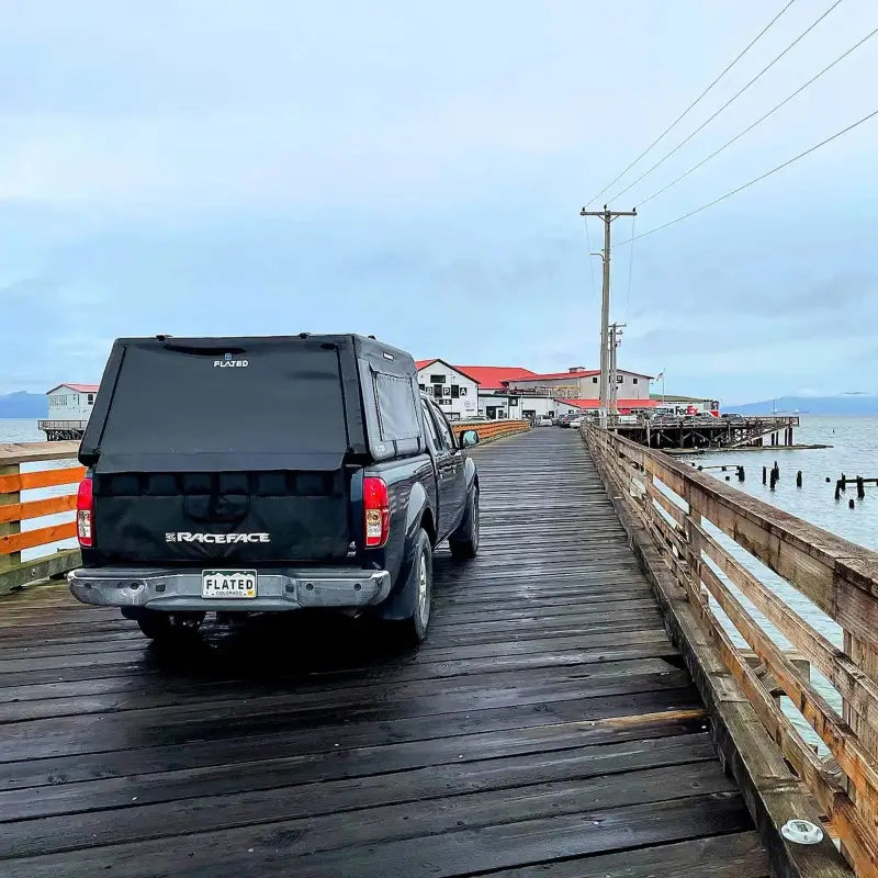 MR - Mid-Size 6'-Long Bed inflatable truck shell on a black truck parked on a wooden pier, emphasizing its durability in various environments.