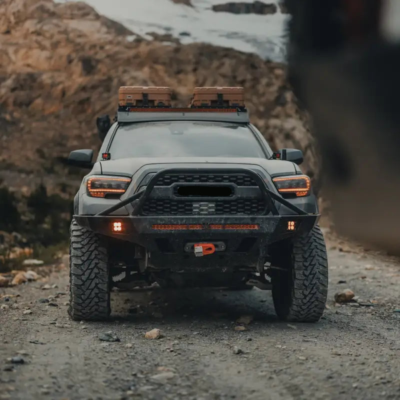 Front view of a 3rd Gen Toyota Tacoma with Overland Front Bumper, winch, and light bar on a rocky trail. Fits 2016+ models.