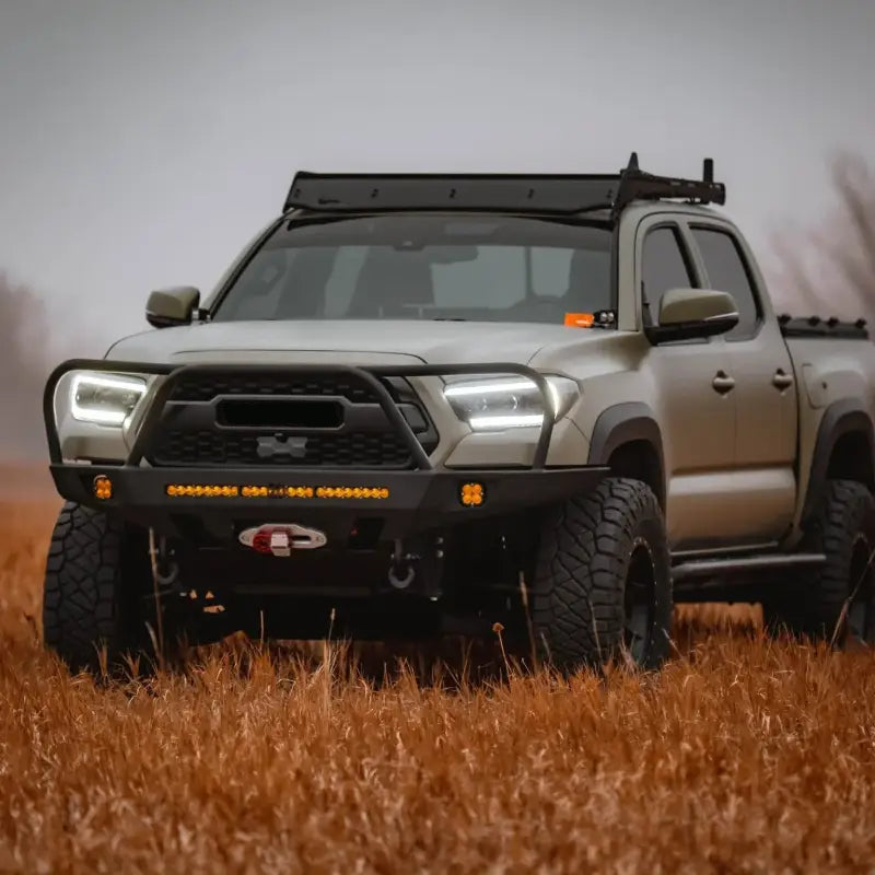 Toyota Tacoma with Overland Front Bumper featuring a winch and 30-inch light bar, parked in a grassy field. Fits 2016+ models.