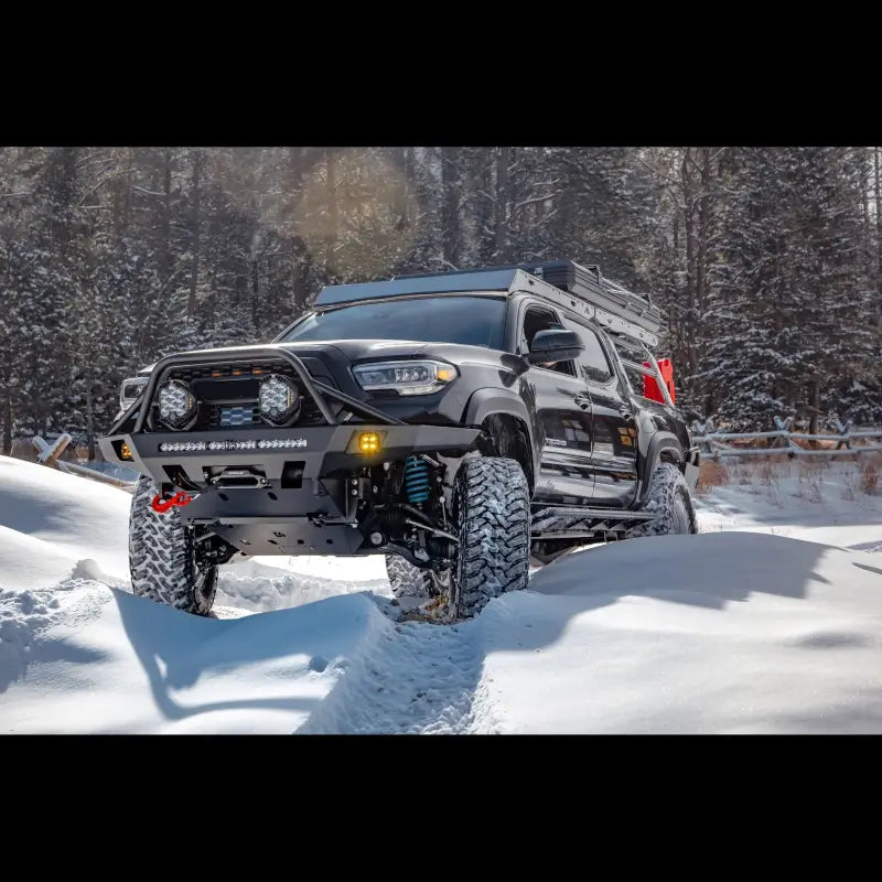 Toyota Tacoma equipped with Overland Front Bumper, winch, and light bar driving through snow in a forest. Fits 2016+ models.