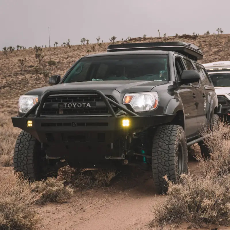Tacoma Overland Series front bumper installed on a 2nd Gen Toyota Tacoma in an off-road desert setting, featuring fog light pockets and heavy-duty design.