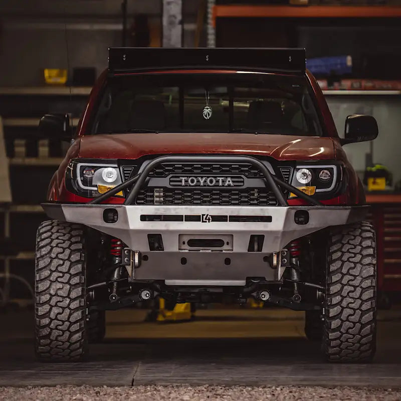 Front view of a red Toyota Tacoma with Tacoma Overland Series front bumper in a garage, highlighting its bolt-on design and rugged construction.