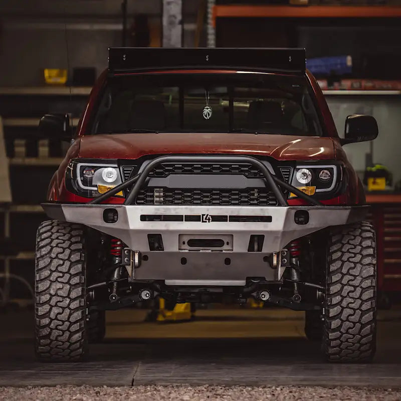 Front view of a red Toyota Tacoma with Tacoma Overland Series front bumper in a garage, highlighting its bolt-on design and rugged construction.