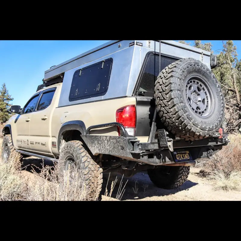 Tacoma Overland rear bumper on a 3rd Gen 2016+ Tacoma with spare tire mount and off-road setup in a forested area.